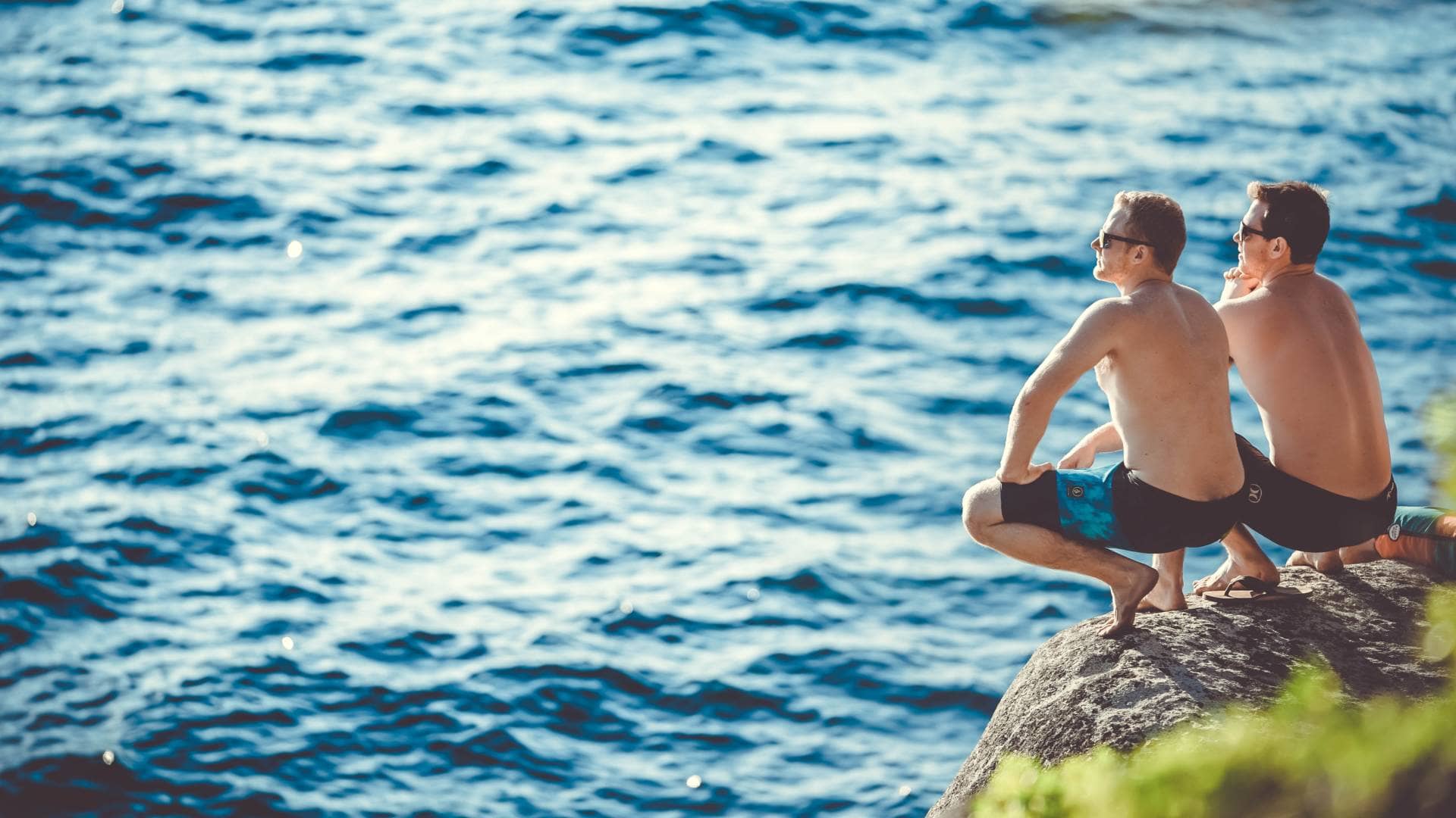 two men sat on a rock by a lake or sea