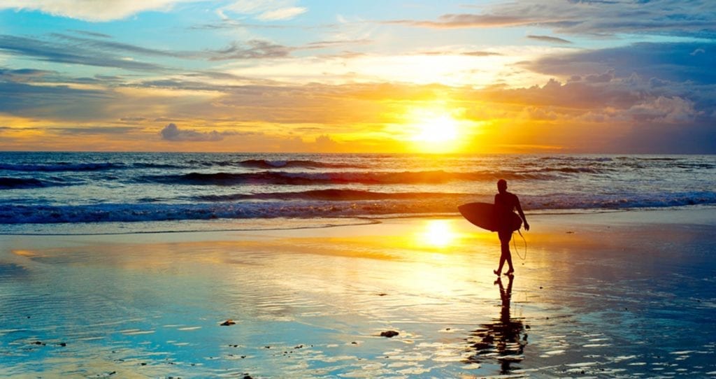 Surfer on the ocean beach at sunset on Bali island, Indonesia;