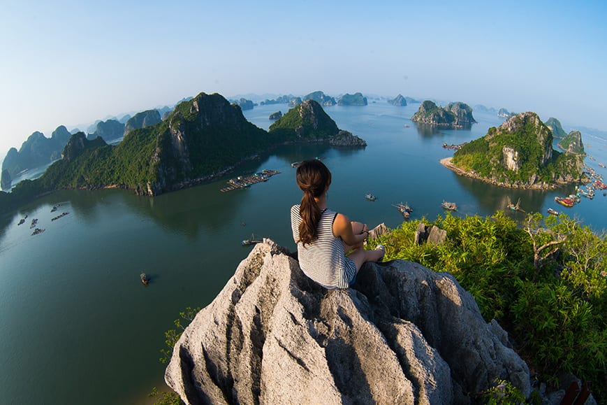 A young traveler girl sit on the top of mountain in Halong bay and enjoy the beauty of seascape. Young girl love wild life, travel, freedom.;