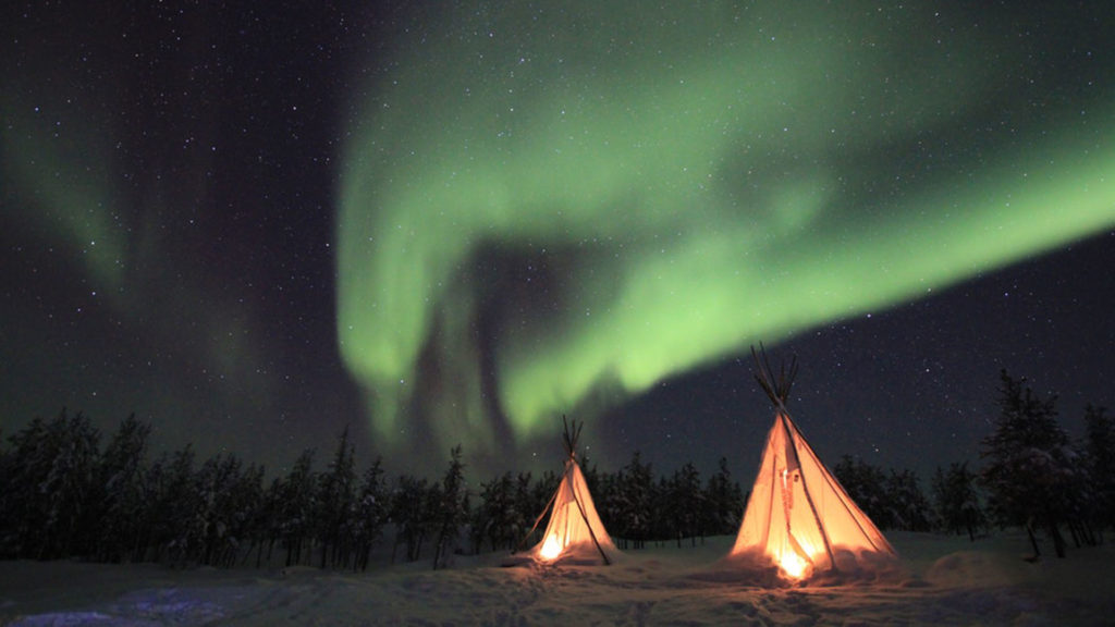 Two wigwam tents lit up by the Northern Lights