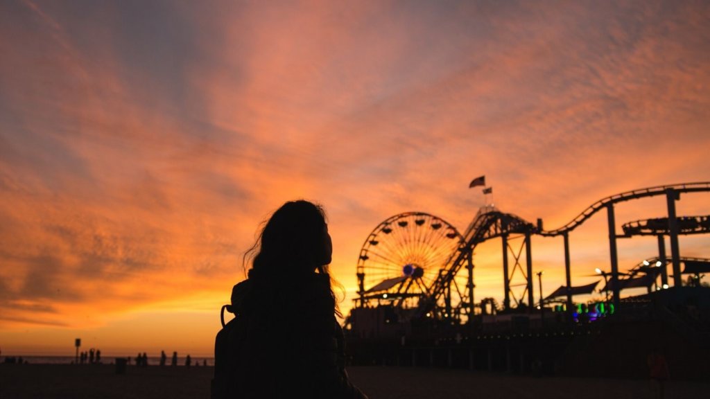 A silhouette of a person in their 30s in front of fairground rides at sunset