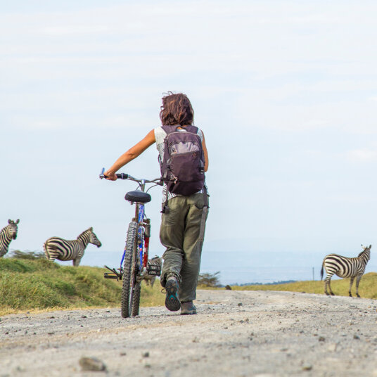 Lady with a bike behind some zebras in the Masai Mara National Park