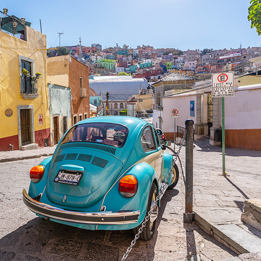 A blue classic VW Beetle driving through the colourful streets of Merida